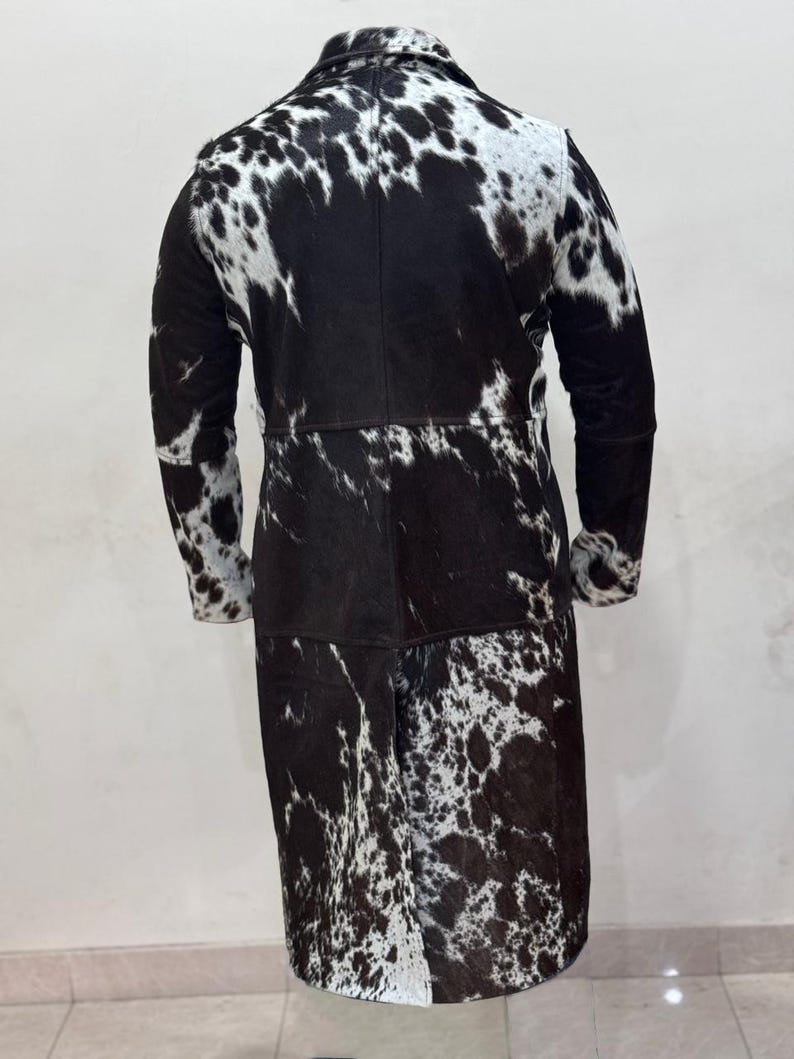 Puede incluir: Un abrigo largo de piel de vaca negro y blanco con manga larga y cuello.
