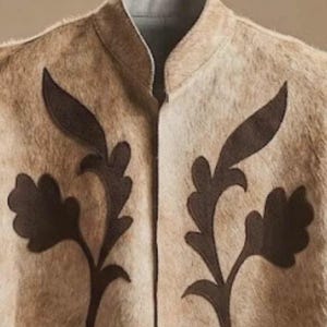 May include: A beige vest with a textured, fur-like appearance featuring a high collar and dark brown, leaf-shaped appliqu&eacute; designs on both sides of the front opening. The garment has a light gray interior lining visible at the neckline.
