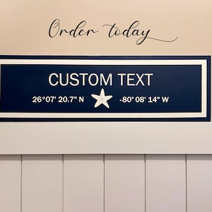 Puede incluir: Un letrero de madera azul marino con texto blanco y una estrella de mar blanca. El letrero dice "CUSTOM TEXT" e incluye las coordenadas "26°07' 20.7" N -80°08' 14" W".