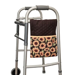 Könnte beinhalten: Eine braune, gesteppte Gehtaschen mit einer Sonnenblumen-Print-Tasche. Die Tasche ist an einem silbernen Gehwagen mit grauen Griffen befestigt. Der Sonnenblumen-Print zeigt gelbe und orangefarbene Blumen mit grünen Blättern auf schwarzem Hintergrund.