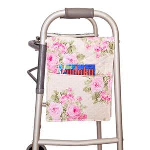 May include: A walker with a floral patterned fabric bag attached to the frame. The bag has a pocket that holds a magazine with the word "Sudoku" on the cover.