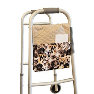 May include: A silver metal mobility walker with a beige quilted fabric pouch attached to the front frame. The pouch features a multi-colored dog breed print and a white rectangular pocket containing a plain white paper insert.