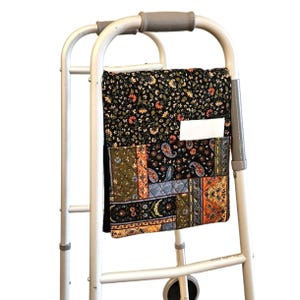 Könnte beinhalten: Ein Gehwagen aus Metall mit grauen Handgriffen verfügt über eine gesteppte Stofftasche, die am vorderen Rahmen befestigt ist. Die Tasche zeigt ein Patchwork-Design mit schwarzen, orangefarbenen, grünen und blauen Blumen- und Paisleymustern sowie einer weißen Tasche.