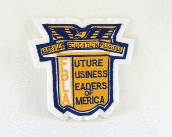 May include: Embroidered patch with the text "SERVICE EDUCATION PROGRESS" and "FUTURE BUSINESS LEADERS OF AMERICA." The patch is shield-shaped with a blue border and gold and blue lettering. An eagle is at the top.