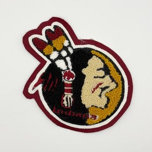 Può includere: Toppa ricamata con un profilo di testa di nativo americano e un copricapo di piume. La toppa ha un bordo bordeaux e la scritta "Indians". Il design incorpora colori neri, oro, rossi e bianchi.