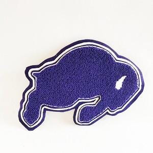 May include: A purple and white embroidered patch in the shape of a buffalo. The patch has a textured appearance and a white outline, with a smaller white detail on the buffalo's body. The background is plain white.