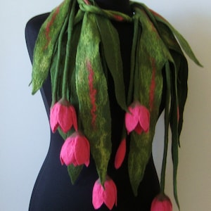 May include: A felted scarf in a tulip design. The scarf features long, green leaves with red accents and vibrant pink tulip blooms. The scarf is draped on a black mannequin, showcasing its shape and texture.