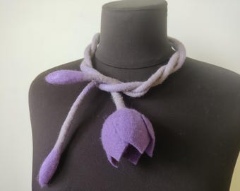 May include: A purple felt flower necklace with a long, thin stem and a large, open flower. The necklace is made of a soft, felted material and is a unique and stylish accessory.