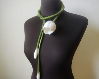 Può includere: Una sciarpa in lana infeltrita verde e bianca, esposta su un manichino nero. La sciarpa presenta un grande fiore di tulipano bianco e due boccioli bianchi. La parte verde della sciarpa è attorcigliata attorno al collo.