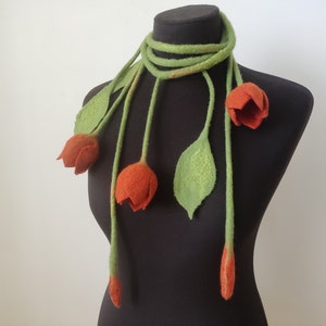 May include: A felt scarf with a floral design. The scarf features orange tulip-shaped flowers, green leaves, and a green stem. The scarf is displayed on a black mannequin. The scarf is a unique accessory.