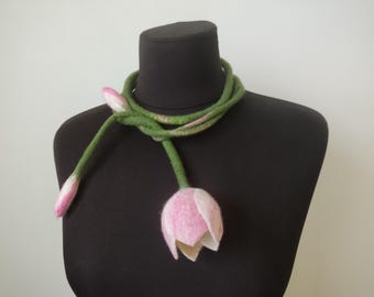 May include: A felted floral necklace featuring a green stem and a pink and white tulip flower. The necklace is displayed on a black mannequin. The flower is made of soft felt material.