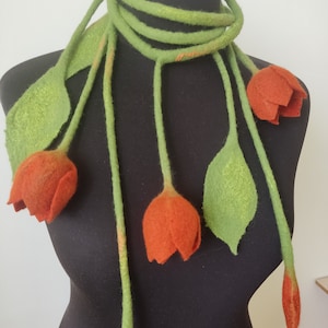 May include: A green felt necklace with five orange felt tulips attached. The necklace is displayed on a black mannequin.