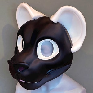 May include: A black and white furry mask with large, rounded ears. The mask has large eye openings and a small nose. The text "EXAMPLE WITH ROUNDED FOAM EARS" is displayed at the bottom of the image. The mask is displayed on a mannequin head.