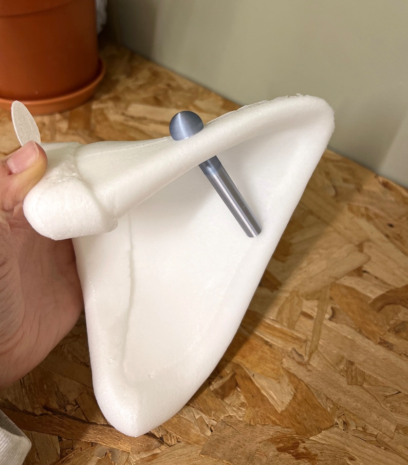 Pode incluir: Um acess&oacute;rio em forma de orelha de espuma branca triangular, com um brinco de pino met&aacute;lico azul-claro liso com uma haste longa e c&oacute;nica. O brinco est&aacute; inserido atrav&eacute;s da parte superior da estrutura branca, curva e em forma de orelha.