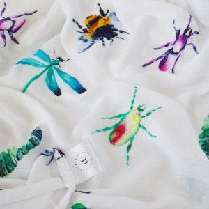 Pode incluir: Tecido branco com uma estampa de aquarela de vários insetos, incluindo uma abelha, uma libélula, uma lagarta e vários besouros. O tecido tem uma textura sutil e um caimento suave e fluido.