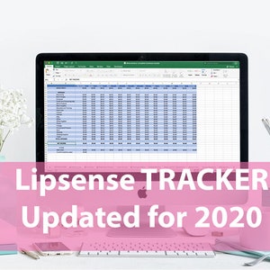 May include: A computer screen displaying a spreadsheet with the title "Lipsense TRACKER Updated for 2020". The spreadsheet is open in a program that looks like Microsoft Excel. The computer is on a white desk with a white flower arrangement, a pink mug, a pink pencil holder, and a silver pencil holder.