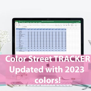 May include: A laptop screen displaying a spreadsheet with the title "Color Street TRACKER Updated with 2023 colors!" The spreadsheet is filled with data and numbers. The laptop is on a white desk with a white flower arrangement, a pink mug, and a silver pencil holder.