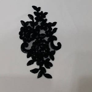May include: A black lace appliqué featuring a floral and leaf pattern with intricate embroidery details. Above the appliqué is a white rectangular business card with the black logo LT and the text LACE TO LOVE printed in a clean, sans-serif font.