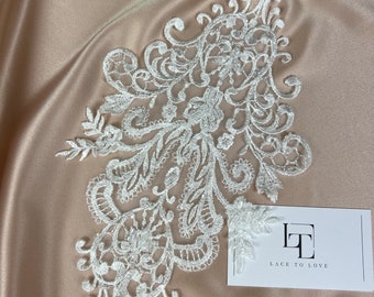 May include: White lace applique with a delicate floral design. The lace is on a beige satin background. The image also includes a business card with the text "Lace to Love".