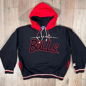 May include: Black Chicago Bulls hoodie with a red hood and accents. The word "Bulls" is in red script across the chest, with "Chicago" above it. Features a drawstring and the Starter logo on the sleeve.