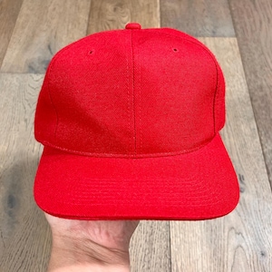 May include: A solid red baseball cap with a curved brim. The cap has a structured crown and a small button on top. The hat is made of a textured fabric.