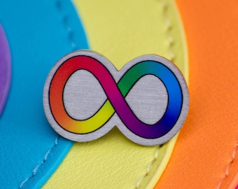 May include: A rainbow infinity symbol pin on a multi-colored background. The pin is silver with a rainbow design.