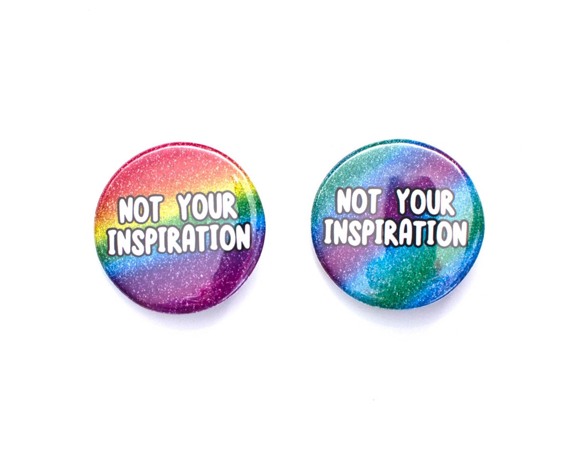 Two rainbow glitter pins with the words "Not your inspiration"
