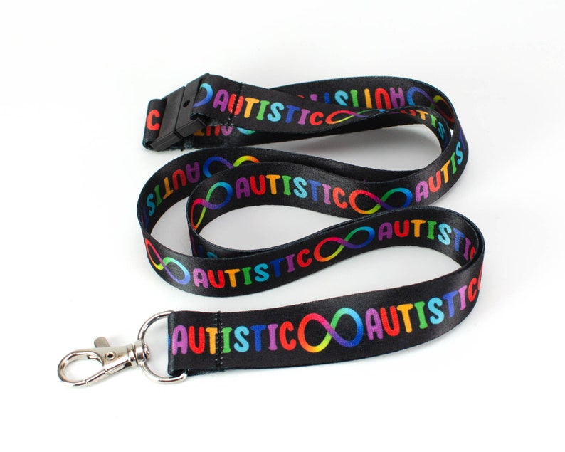 May include: Black lanyard with a rainbow infinity symbol and the word "AUTISTIC" repeated along the length. The lanyard has a silver clip.