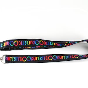 May include: Black lanyard with a repeating pattern of the word "autistic" and an infinity symbol in rainbow colours.