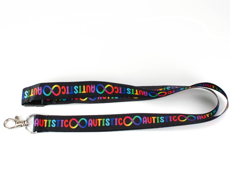 May include: Black lanyard with a repeating pattern of the word "autistic" and an infinity symbol in rainbow colours.