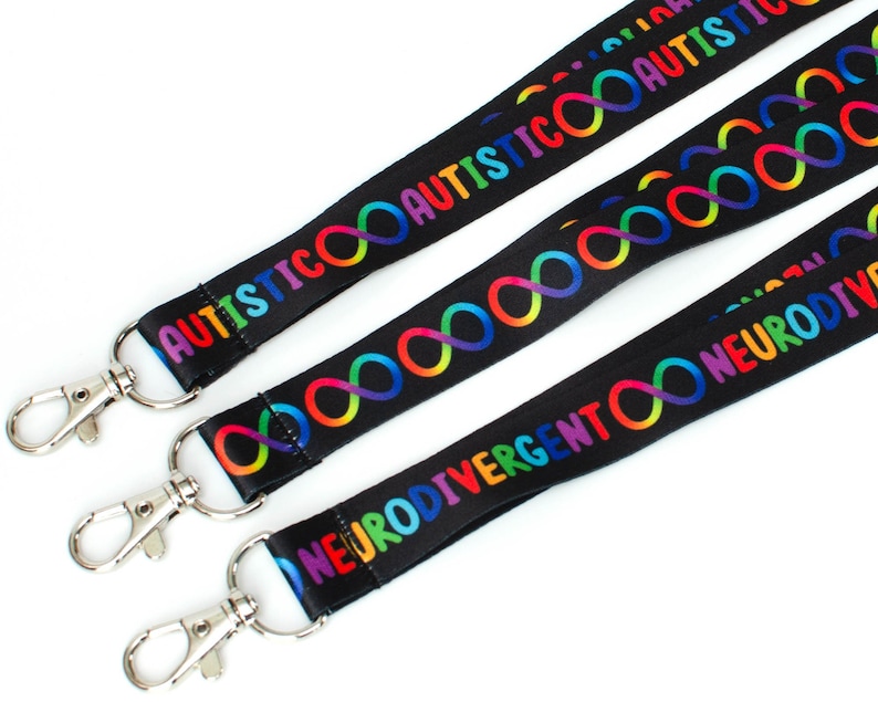 May include: Three black lanyards with rainbow infinity symbols and text. The lanyards have silver clips. The text on the lanyards reads "AUTISTIC", "AUTISTIC", and "NEURODIVERGENT".