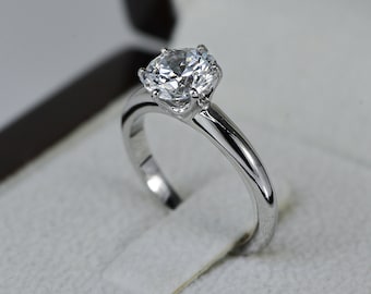 May include: A silver engagement ring with a large, round, clear diamond in a box.