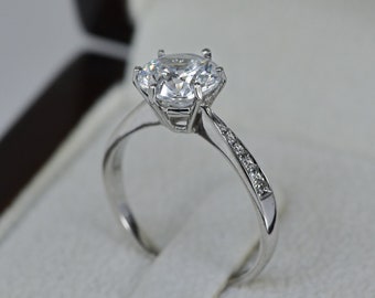 May include: A silver engagement ring with a large, clear, round-cut diamond center stone and smaller diamonds set in a band.