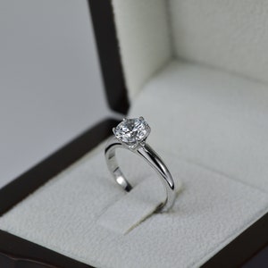 May include: A silver engagement ring with a large, round, clear diamond in a black ring box.