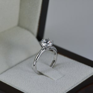 May include: A silver engagement ring with a large, round, clear diamond in a black ring box.