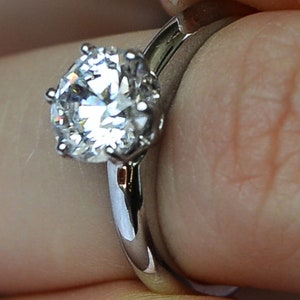 May include: A silver engagement ring with a large, round, clear diamond.