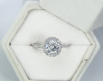 May include: A silver engagement ring with a large, round, clear diamond surrounded by a halo of smaller diamonds.