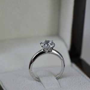 May include: A silver engagement ring with a large, round, clear diamond in a classic setting.