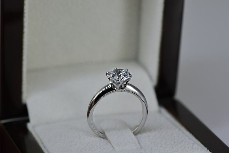 May include: A silver engagement ring with a large, round, clear diamond in a classic setting.
