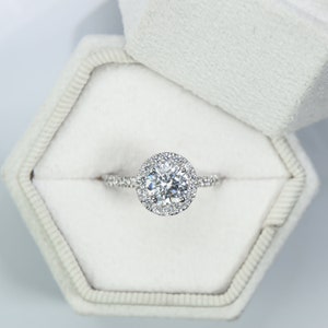 May include: A silver engagement ring featuring a large, round, clear diamond with a halo of smaller diamonds.