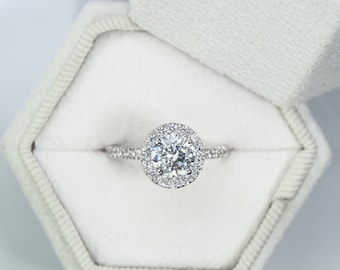 May include: A silver engagement ring with a large, round, clear diamond surrounded by a halo of smaller diamonds.