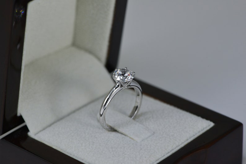May include: A silver engagement ring with a large, round, clear diamond in a black ring box.