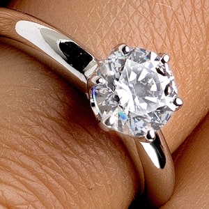May include: A silver engagement ring with a large, round, clear diamond.