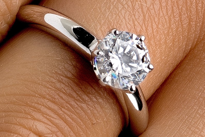 May include: A silver engagement ring with a large, round, clear diamond.