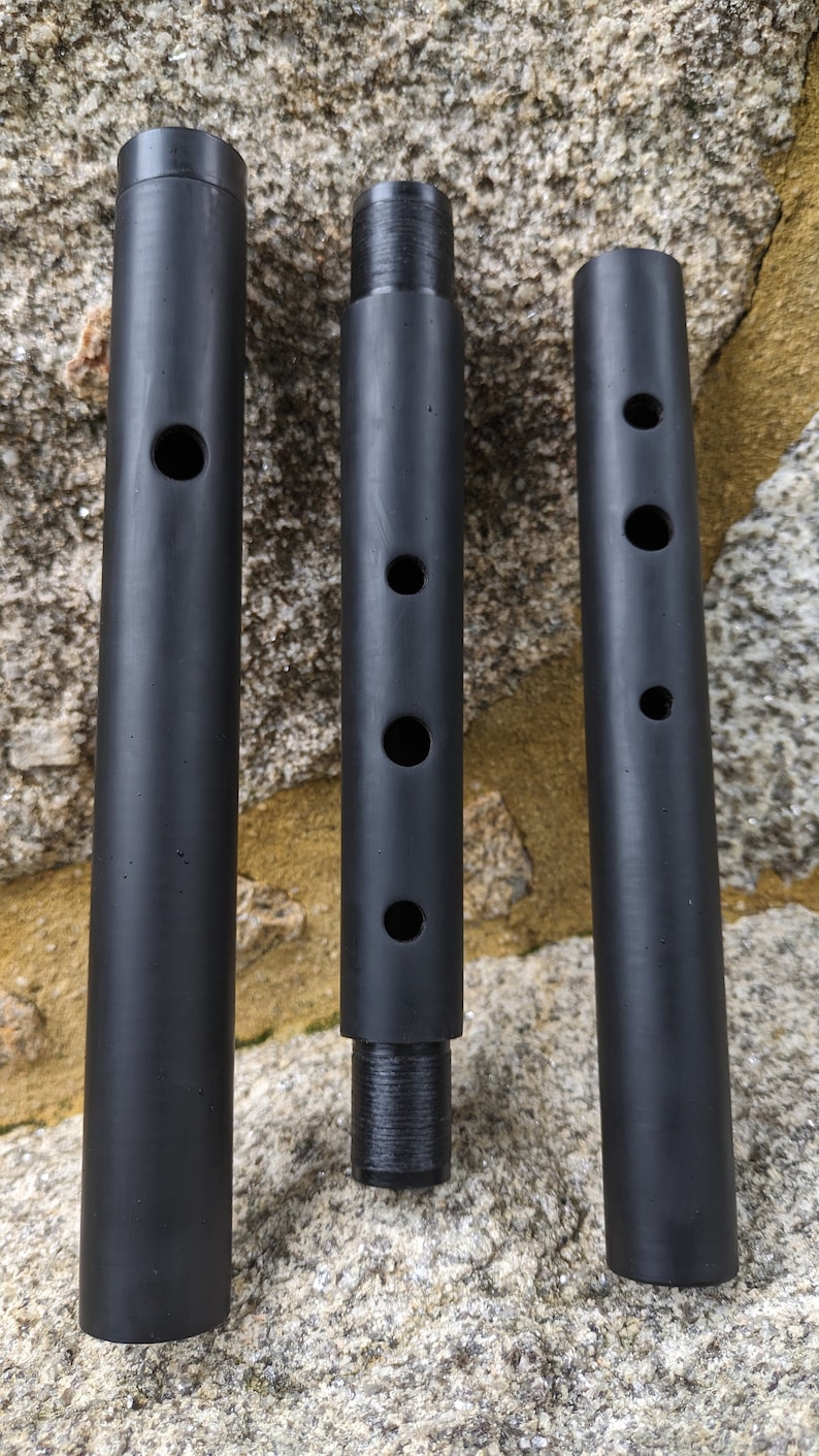 May include: Three black cylindrical tubes with different numbers of holes drilled into them. The tubes are made of a smooth, black material and are arranged in a row from left to right.