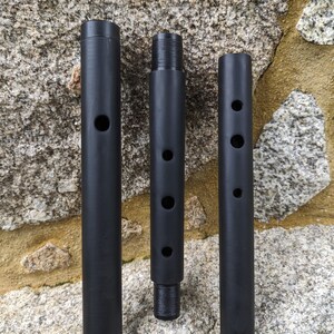 May include: Three black metal rods with holes drilled into them. The rods are arranged vertically against a stone background.