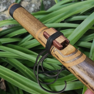 Pode incluir: Uma flauta de madeira com acabamento marrom, preto e marrom claro. A flauta tem uma alça de couro e um bocal de madeira. A flauta é feita de várias peças de madeira que são unidas.