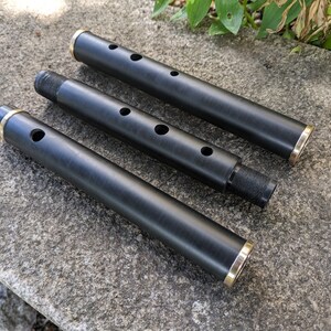 May include: Three black wooden flutes with gold accents. The flutes are of different lengths and have multiple finger holes.