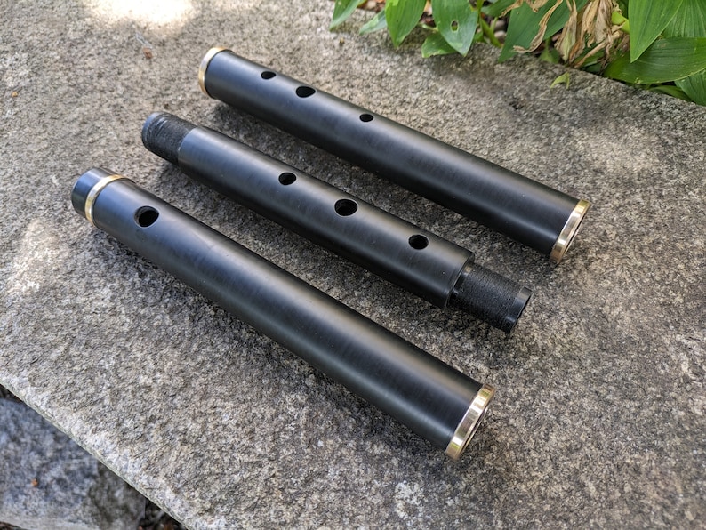 May include: Three black wooden flutes with gold accents. The flutes are of different lengths and have multiple finger holes.