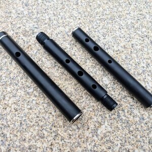 May include: Three black metal pipes with silver accents. The pipes are different lengths and have holes along the side.